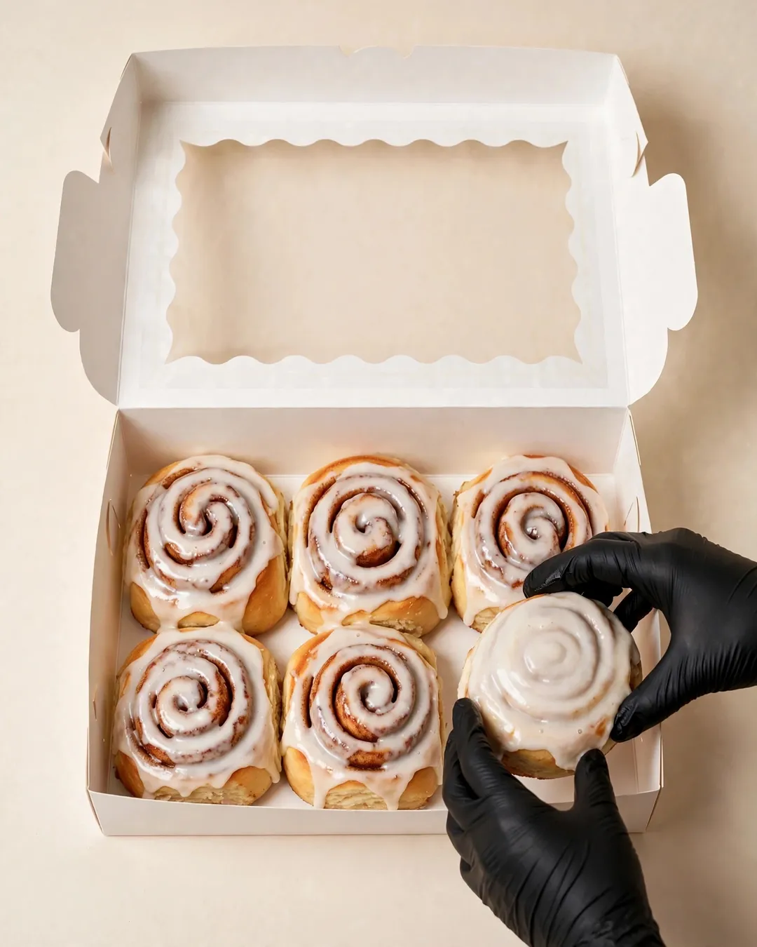 Gloved hands placing a glazed cinnamon roll into a bakery box
